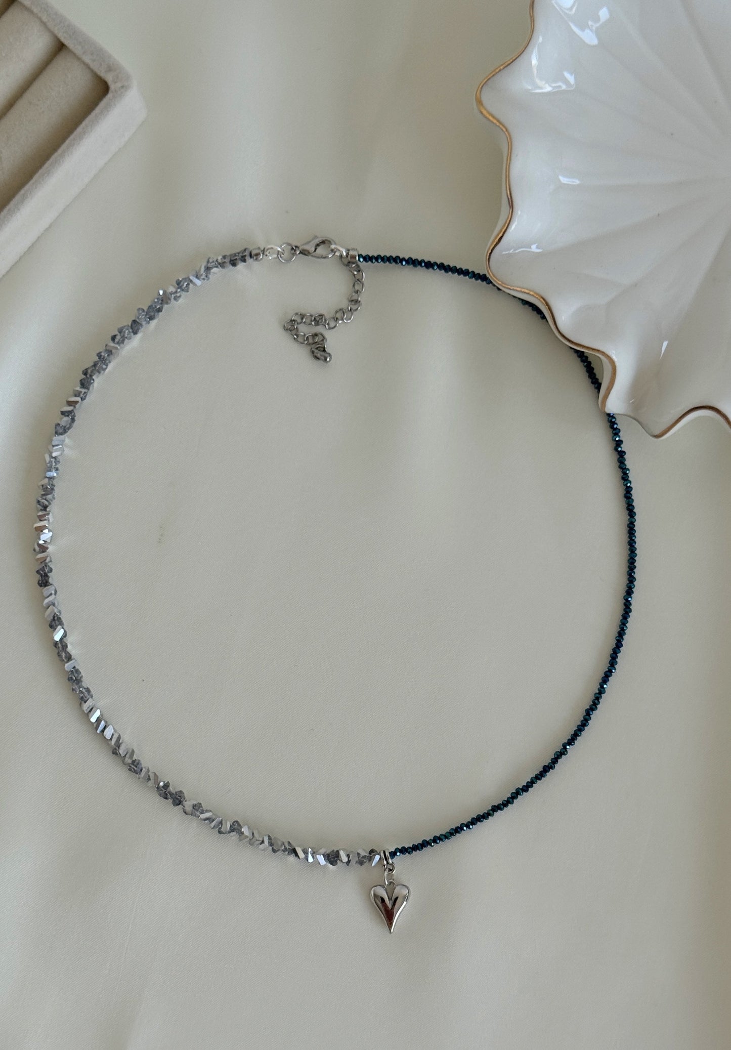Asymmetrical necklace featuring metallic hematite chips and navy crystal beads with a dangling heart charm
