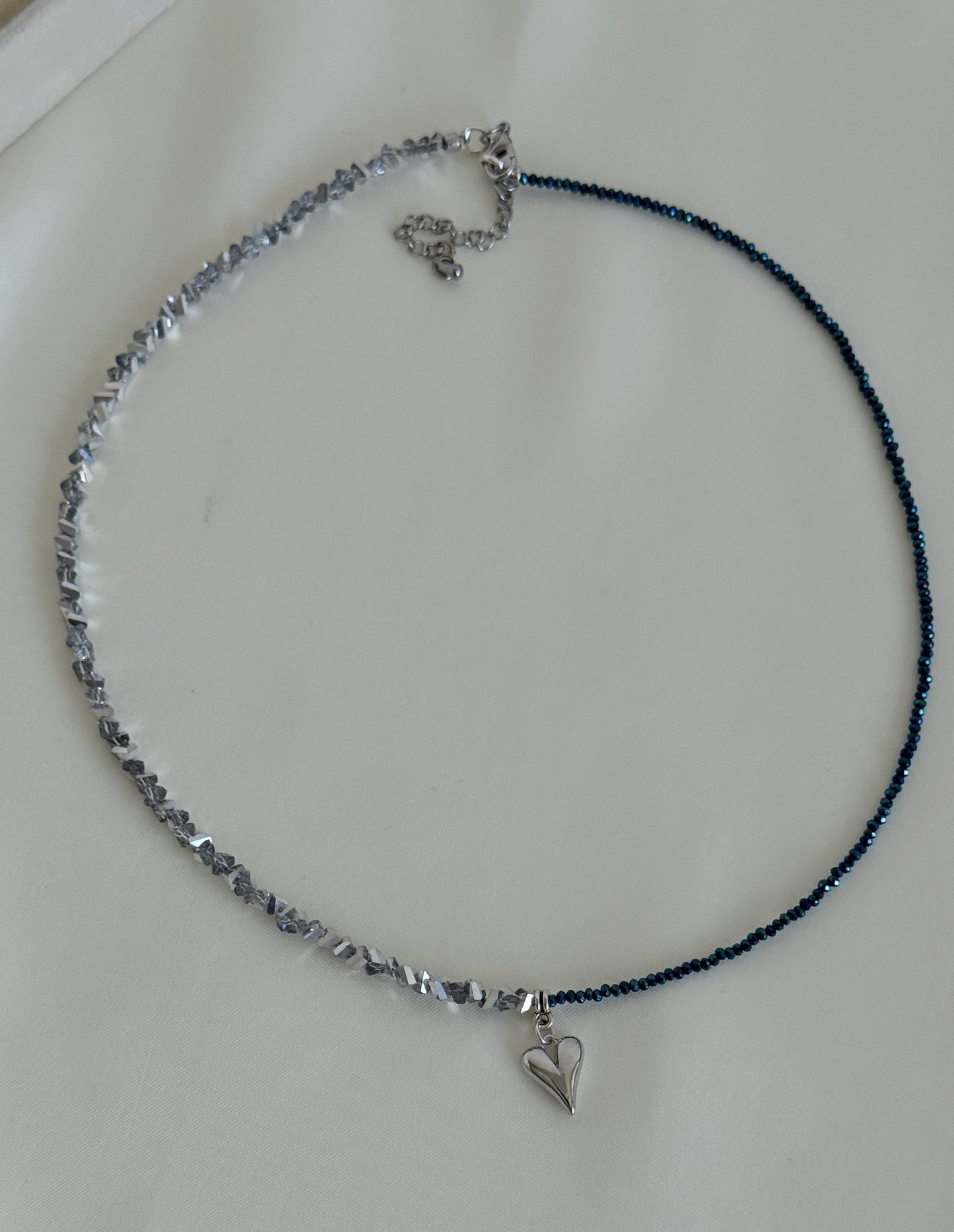 Close-up of handmade hematite and blue crystal necklace with a small silver heart charm in the center