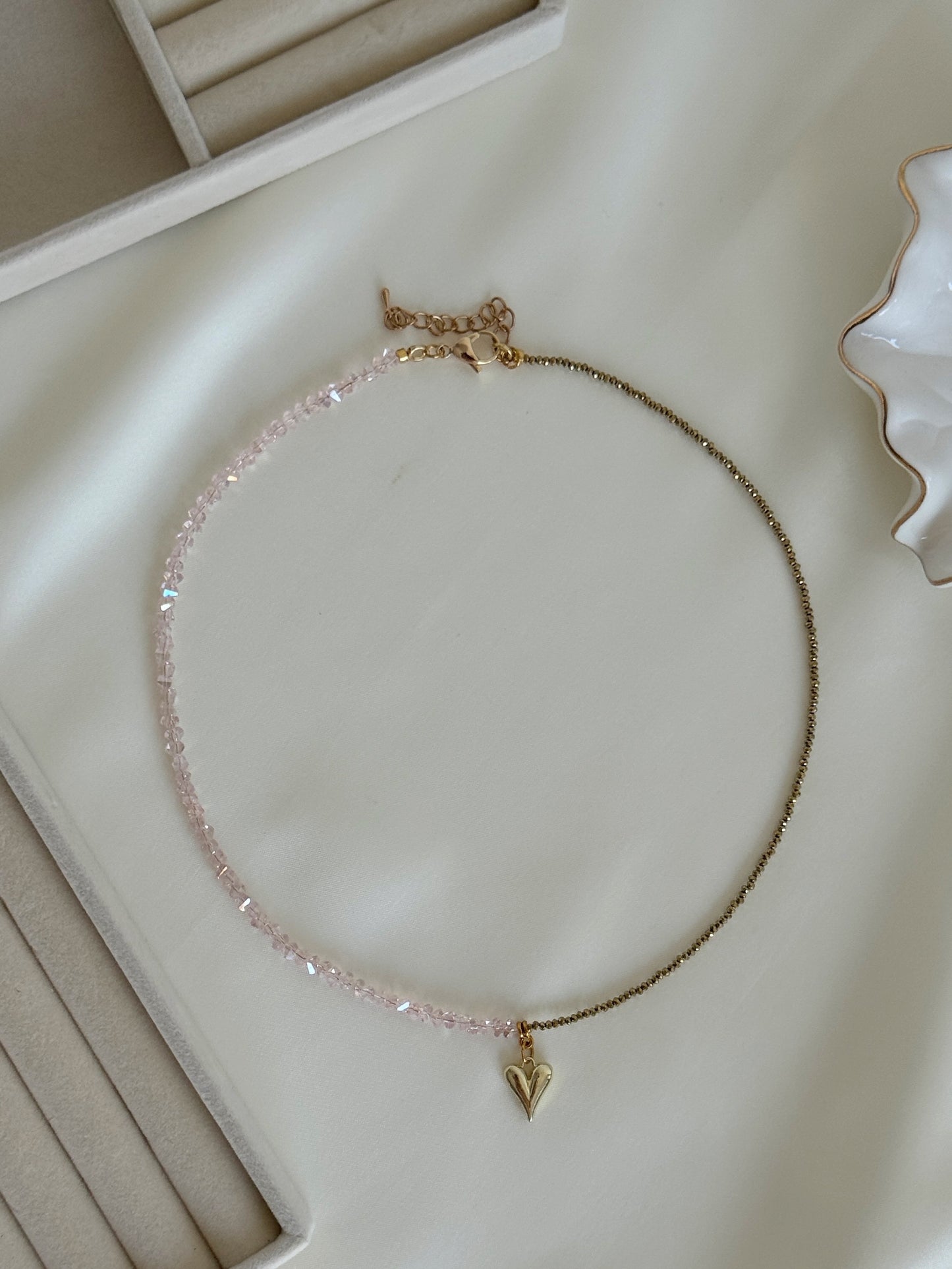 Layered pink crystal and gold hematite necklace arranged neatly on a soft fabric