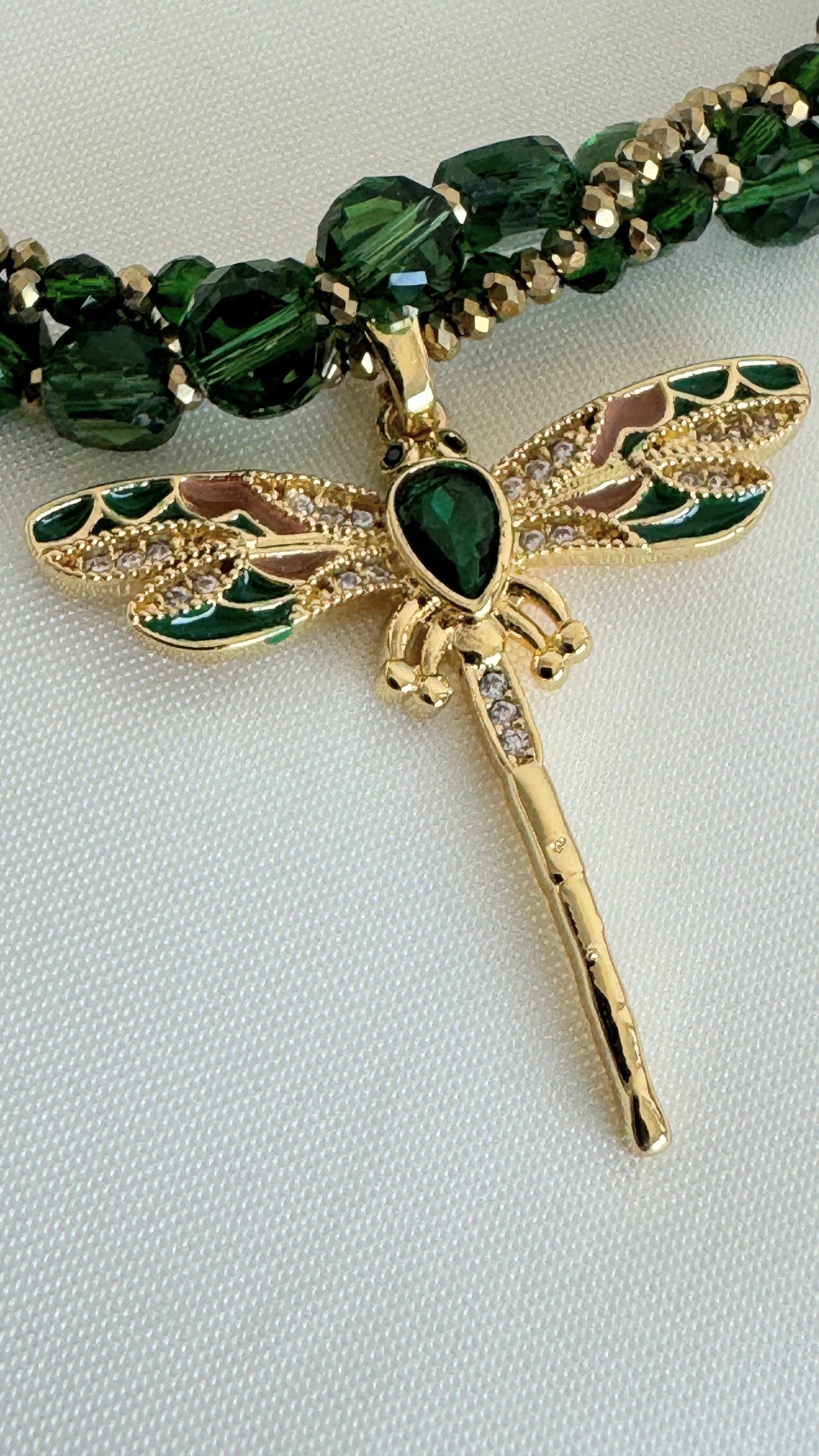 Close-up of green crystal beads and gold dragonfly pendant on necklace