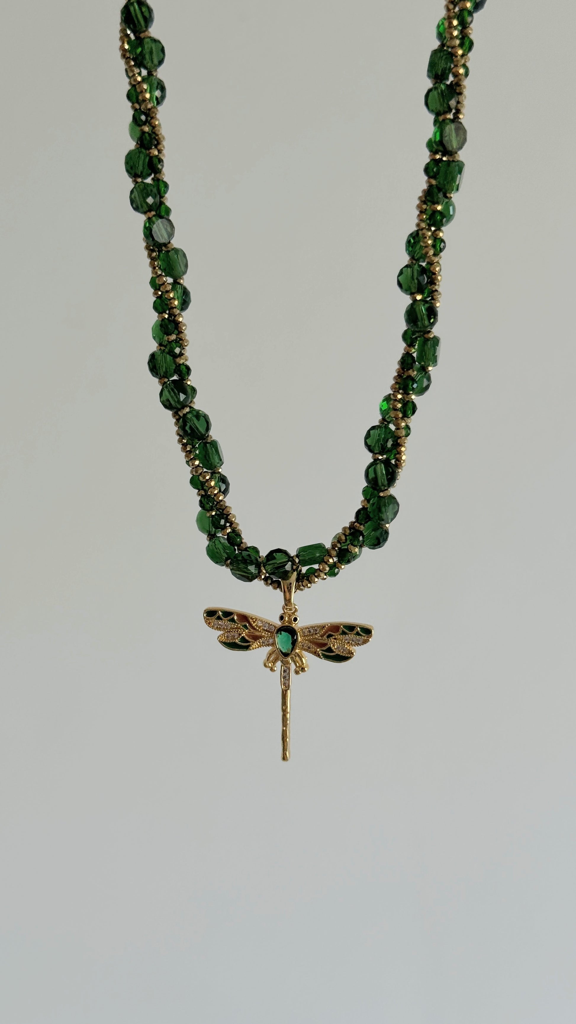 Elegant green crystal necklace with gold dragonfly displayed on jewelry stand