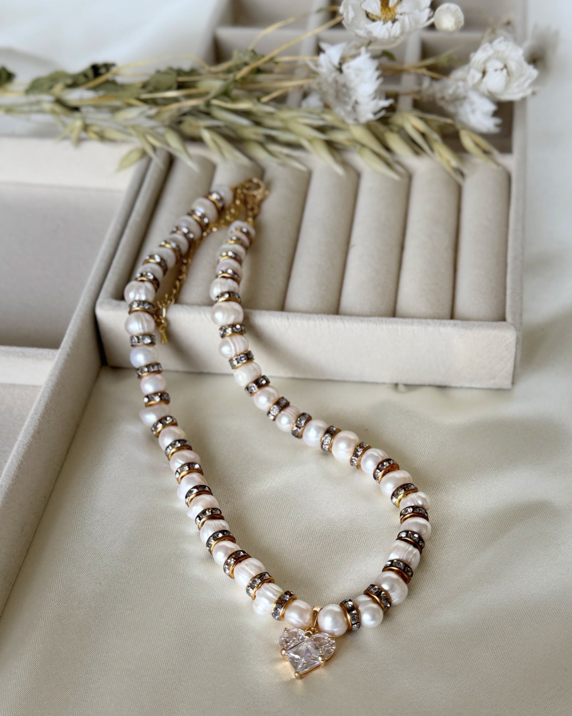 Pearl necklace with crystal heart pendant and gold accents on white background