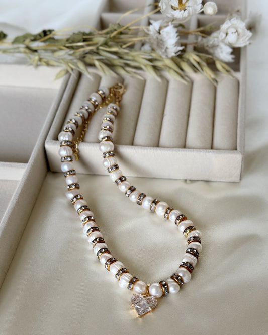 Pearl necklace with crystal heart pendant and gold accents on white background