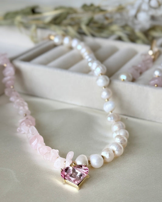 Pink quartz crystal and pearl necklace with gold accents on white background