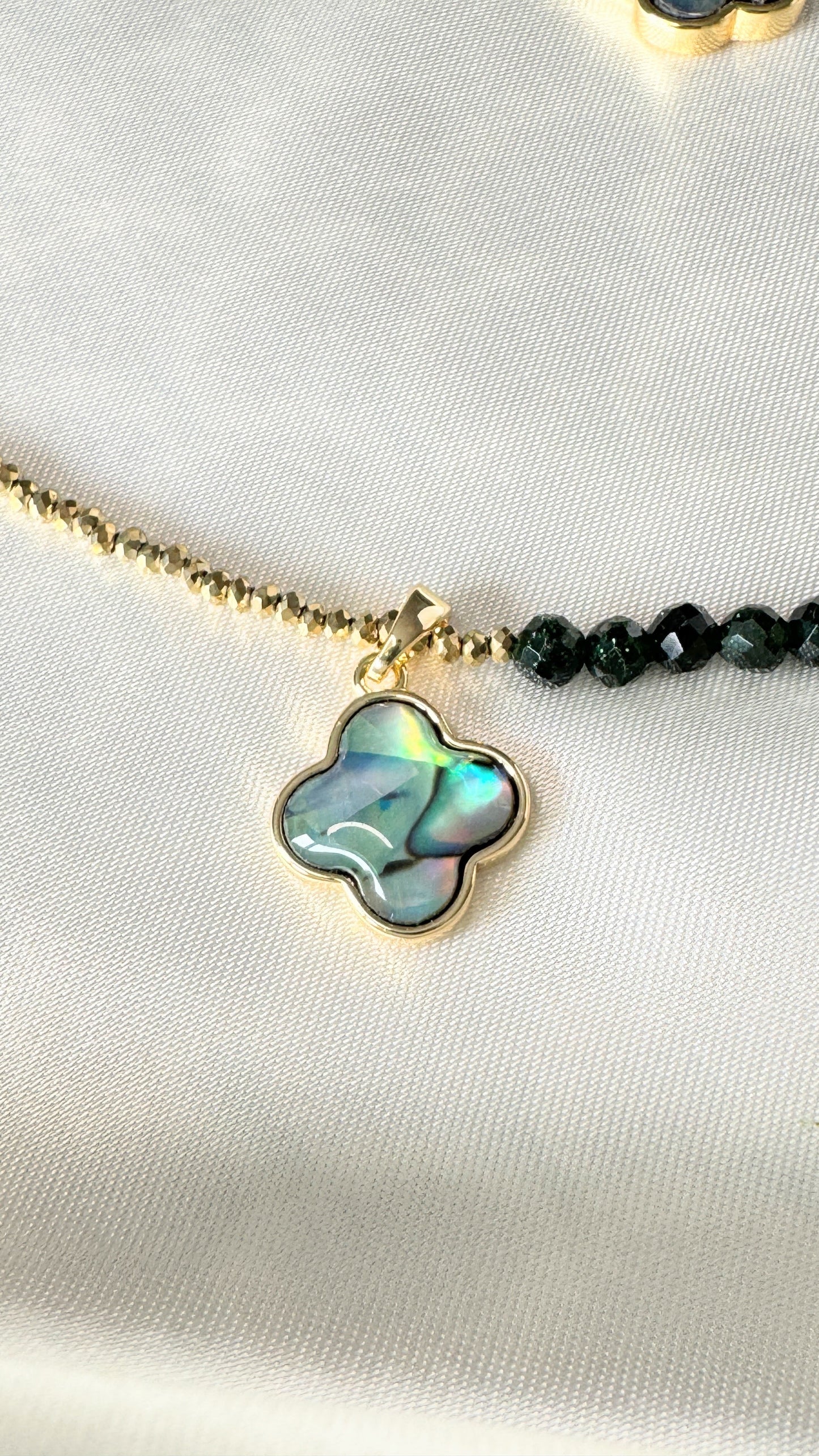 Close-up of hematite beads and crystal clover pendant on gold necklace
