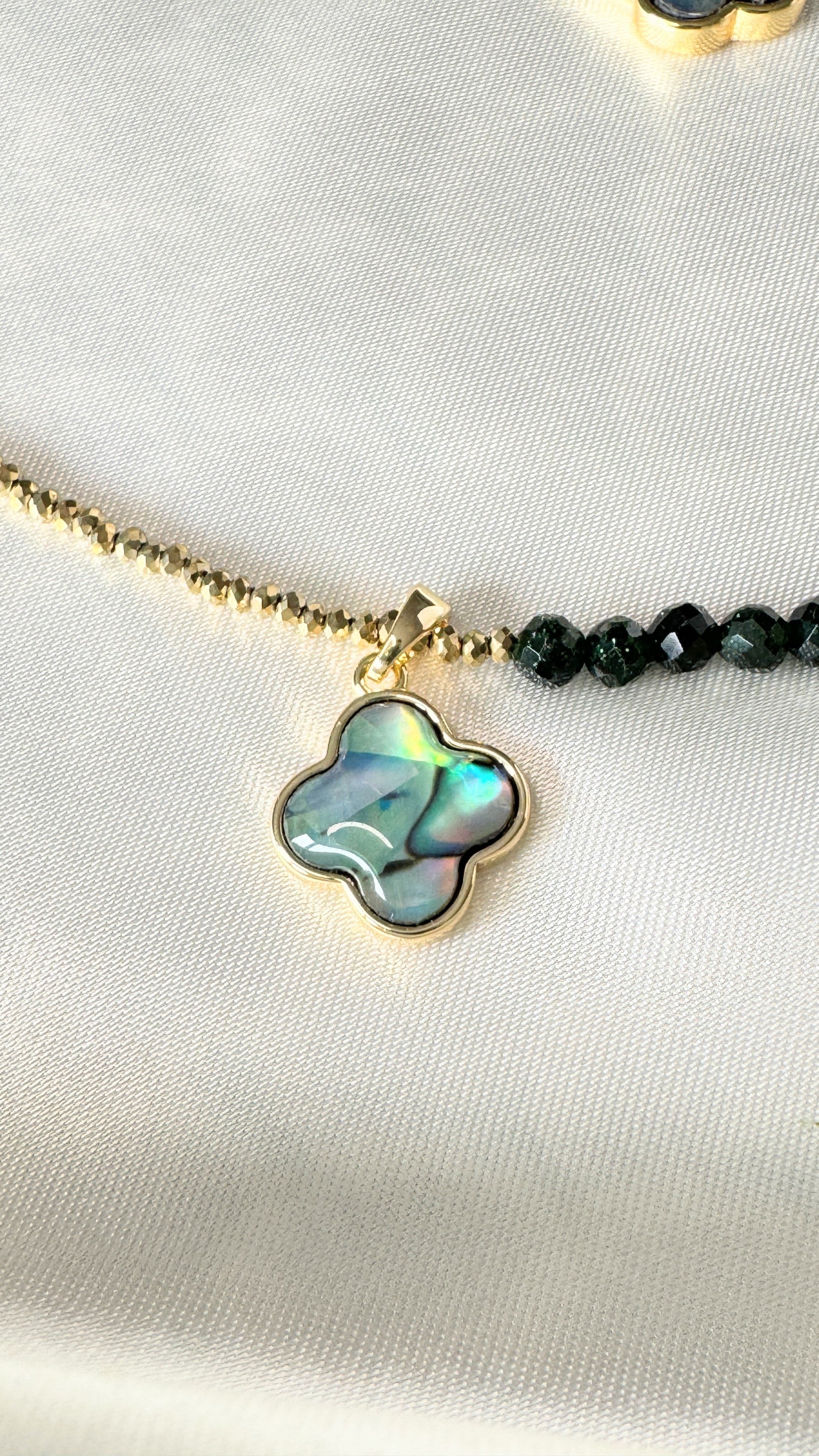 Close-up of hematite beads and crystal clover pendant on gold necklace