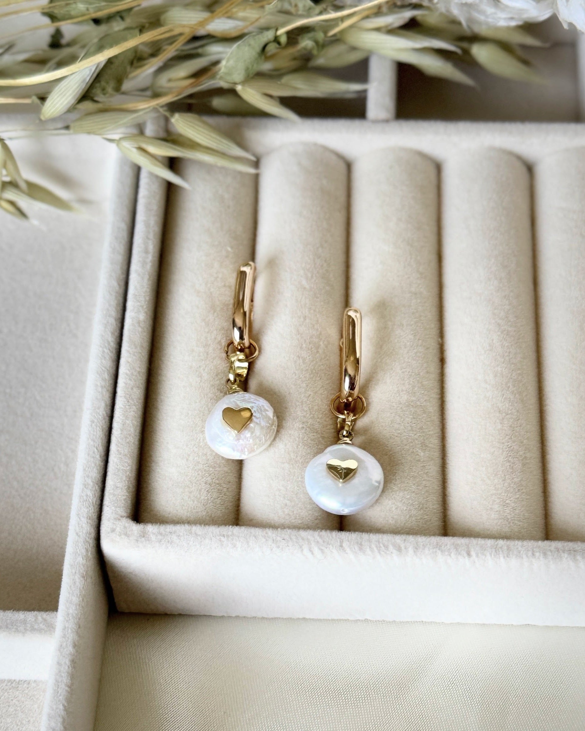 Close-up of dangling heart pearl earrings with gold details