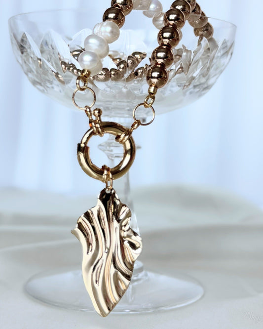 Golden hematite pearl necklace with layered gold chains on white background