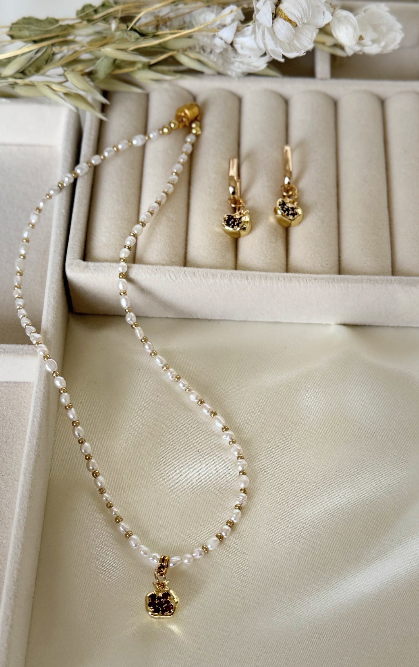 Golden pomegranate pearl necklace displayed on soft fabric background