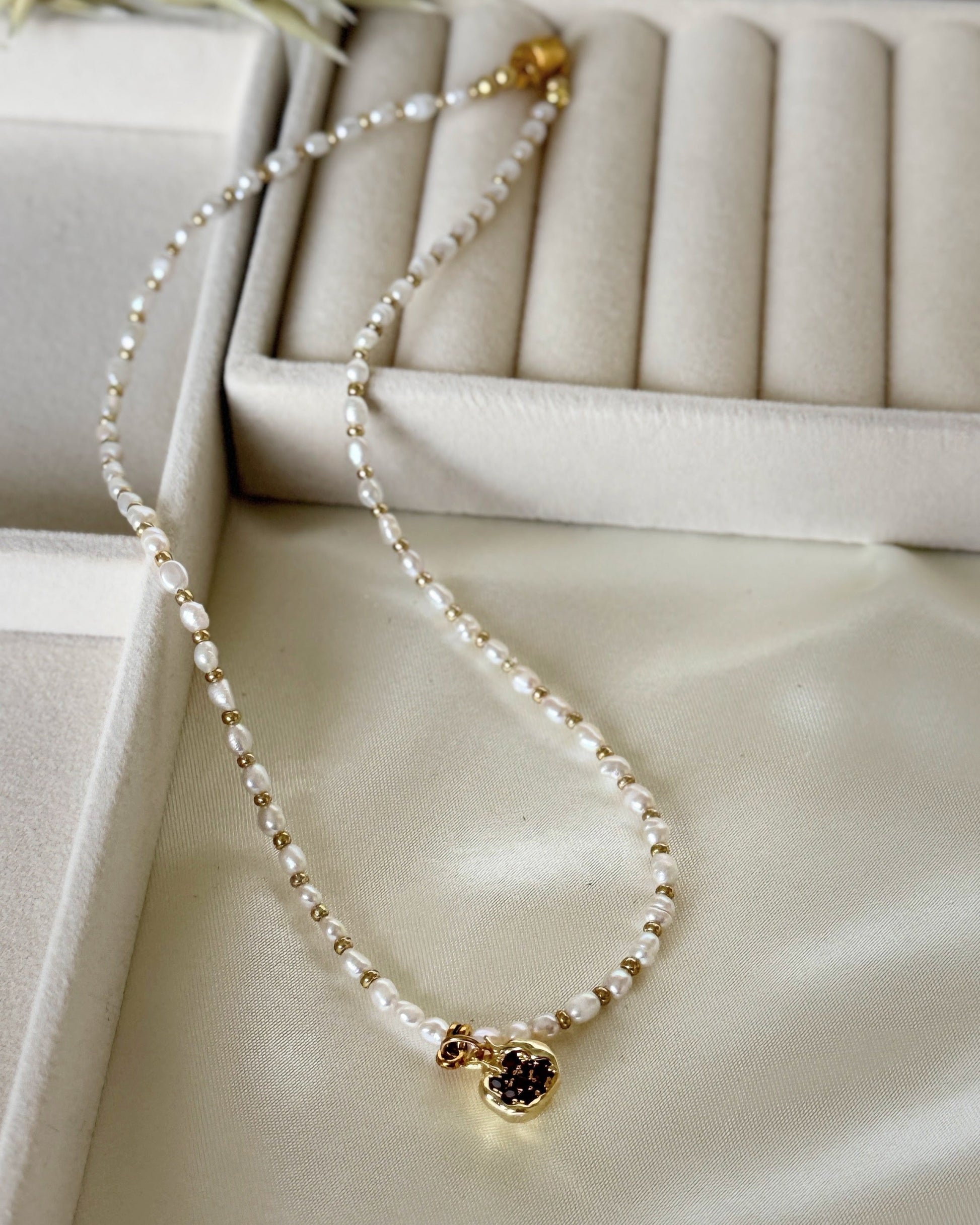 Golden pomegranate pearl necklace with layered gold chain on white background
