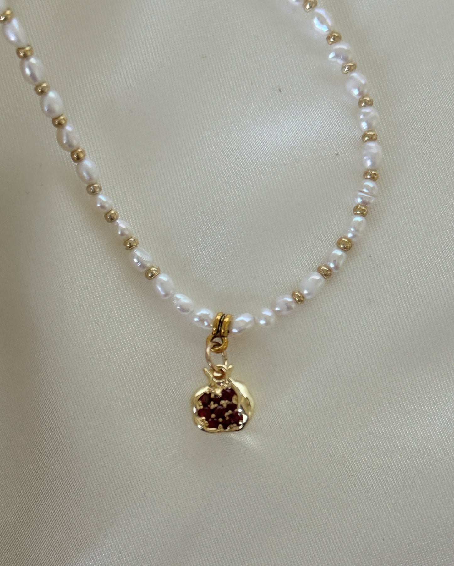 Close-up of golden pomegranate charm and freshwater pearls on necklace