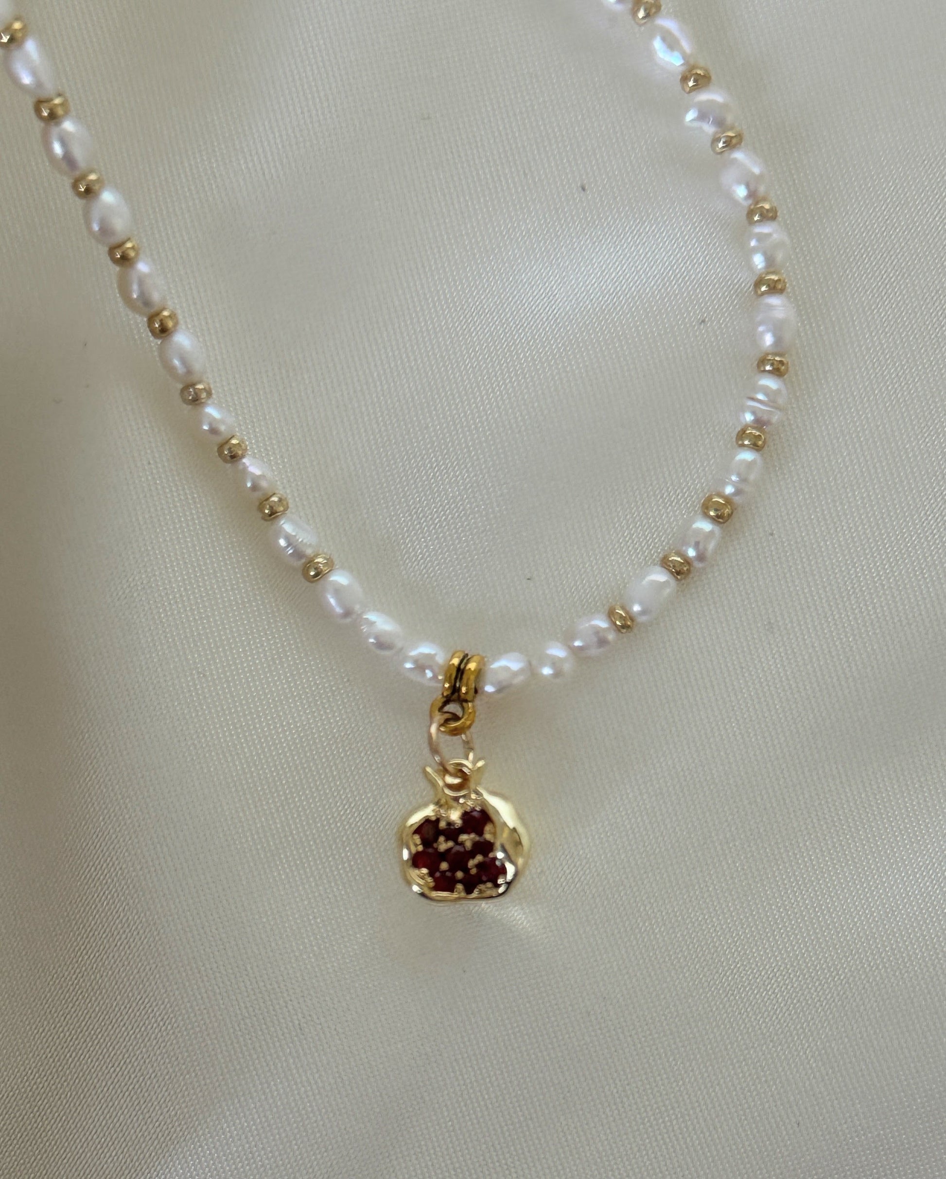 Close-up of golden pomegranate charm and freshwater pearls on necklace