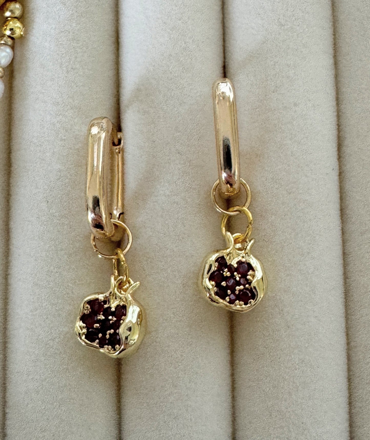 Close-up of dangling golden pomegranate earrings with garnet charms