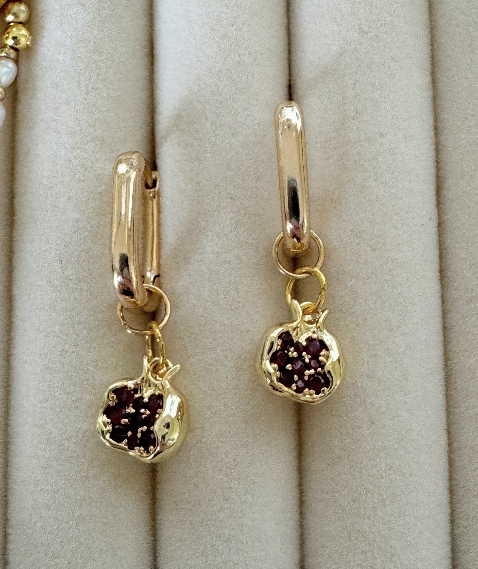 Close-up of dangling golden pomegranate earrings with garnet charms